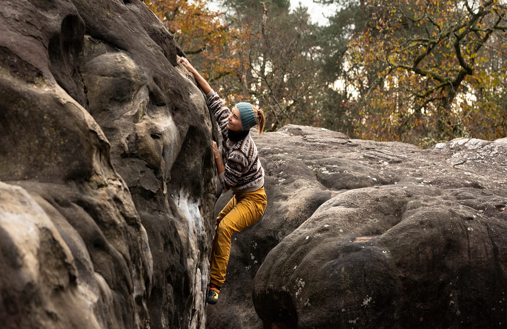 Woman climbing a rock face in a forest during autumn.