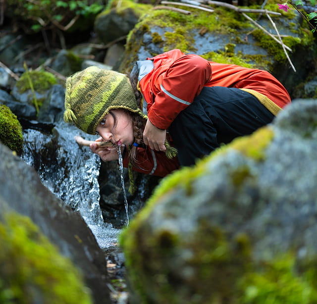 Patagonia Action Works - community member drinking water from a mountain stream in a forest.
