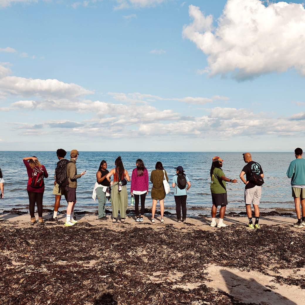 Diverse group of outdoor community members gathered on a beach overlooking the sea.